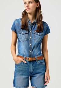 Vestido de camisa de denim con mangas cortas, parte delantera con botones y dos bolsillos en el pecho. Tela de color azul claro, complementada con un cinturón marrón con hebilla de metal.