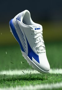 White athletic shoe with blue accents, textured upper, and spikes on the sole; raised design lines and logo on the side.