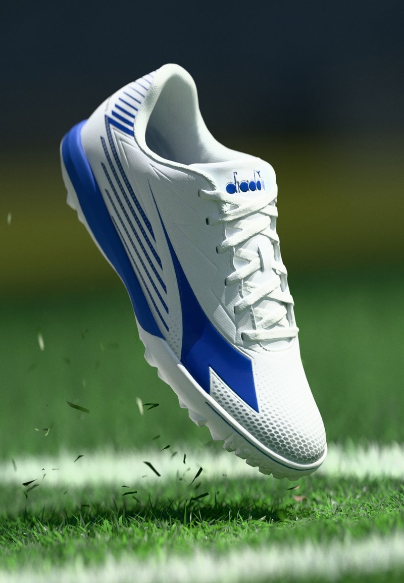 White athletic shoe with blue accents, textured upper, and spikes on the sole; raised design lines and logo on the side.