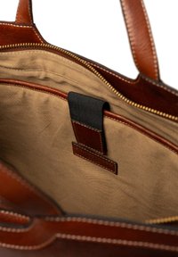 Indvendig i en brun læder tote bag med beige stofforing, har en lomme med en sort rem og kontrasterende syninger langs kanterne.