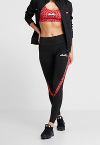 Roter Leoparden-Print Sport-BH mit schwarzen, hoch taillierten Leggings, die rote Seitenstreifen und einen elastischen Bund aufweisen. Schwarze Sportschuhe.