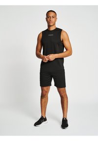 Zwarte mouwloze sporttop en shorts, gemaakt van ademend materiaal. De top heeft een klein logo en is gecombineerd met zwarte sportschoenen.