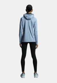 Ljusblå idrottshoodie med en åtsittande design, grå detaljer och huva. Kombineras med svarta leggings och flerdimensionella löparskor.