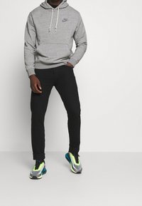 Šedá mikina s žebrovanými manžetami a šňůrkami, v kombinaci s černými slim-fit džíny a vícebarevnými sportovními botami s síťovaným designem.