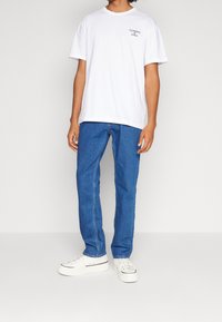 Camiseta de algodón blanca con el logo "TOMMY JEANS", combinada con jeans de mezclilla azul y zapatillas blancas. Diseño sencillo, ajuste relajado.