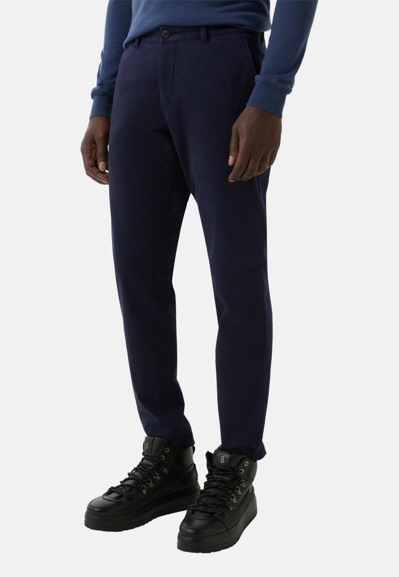 Navy blue cotton chinos with a straight leg, side pockets, and a button closure, paired with black high-top sneakers.