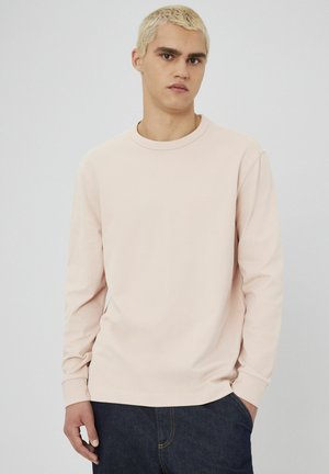 Chemise à manches longues rose clair en tissu lisse avec un col rond. Le design présente des poignets ajustés et une coupe décontractée.