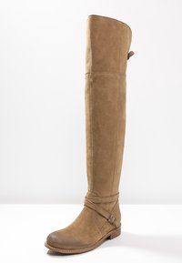 Knee-high brown suede boot with a rounded toe, strap detail with a buckle, and a flat sole, featuring a smooth texture and clean lines.