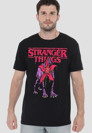 Black cotton T-shirt featuring a vibrant pink "Stranger Things" logo and a graphic of a stylized creature in purple with a red accent.