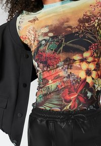 Langærmet top med blomstermønster i livlige farver, med rund halsudskæring og tætsiddende silhuet. Parret med en sort jakke.