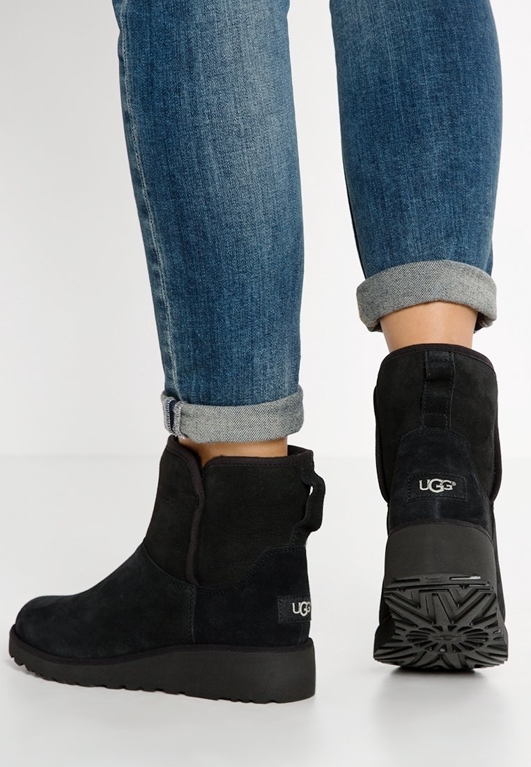 Botas de tobillo de ante negro con punta redondeada, logo en el talón y suela de goma texturizada. Llevadas con jeans de mezclilla enrollados.