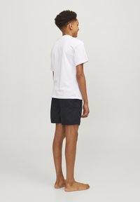 Camiseta blanca de algodón y pantalones cortos azul marino, mostrados desde la parte de atrás. La camiseta tiene un cuello redondo; los pantalones cortos cuentan con un bolsillo trasero y un diseño sencillo.
