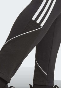 Zwarte sportbroek met witte strepen, gestructureerde zijkanten en contrasterende witte accenten langs de naden. Gemaakt van rekbare stof.