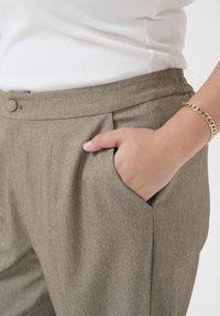 Taupe trousers in a textured fabric with a flat front, side pockets, and a smooth waistband. Paired with a white fitted top.