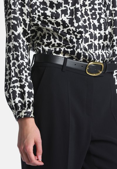 Blouse à manches longues à motif noir et blanc rentrée dans un pantalon noir avec une ceinture en cuir noire ornée d'une boucle ovale dorée.
