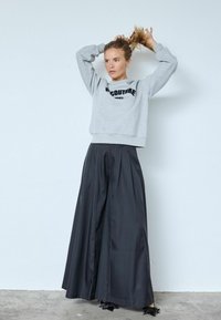 Szürke rövidített pulóver "COUTURE" felirattal, fekete magasderekú, pliszírozott, bő szárú nadrággal, melynek szegélyén texturált díszítések találhatók.