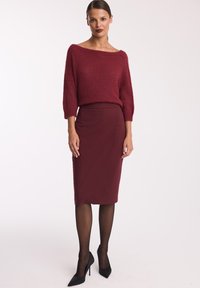 Bordowy sweter dzianinowy z szerokim dekoltem i rękawami do łokci, w połączeniu z dopasowaną bordową spódnicą. Czarne szpilki dopełniają wygląd.