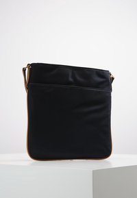 Borsa a tracolla nera in nylon con una texture liscia, caratterizzata da un rivestimento in pelle marrone e una forma semplice e rettangolare. Inclusa tracolla regolabile.