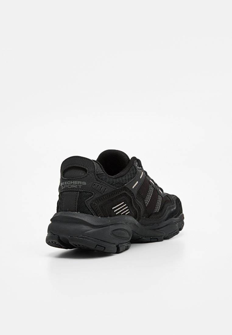 Baskets de sport Skechers noires avec tige en maille et synthétique, col rembourré, semelle texturée et accents réfléchissants. La vue arrière montre le détail du logo.