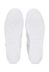 Paire de semelles de baskets blanches vues de dessous, avec des motifs de semelle texturés et géométriques et une zone rectangulaire pour le logo près des talons.