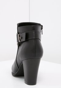 Black leather ankle boot with a high heel, featuring a side zipper and a wide strap with metal buckle detail. Smooth texture and structured shape.