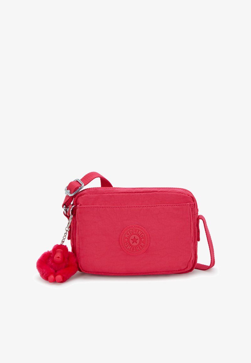 Kompakt, lyserød nylon crossover-taske med struktureret overflade, der har et logo-patch på fronten og en rød, fluffy abe-nøglekæde som tilbehør.