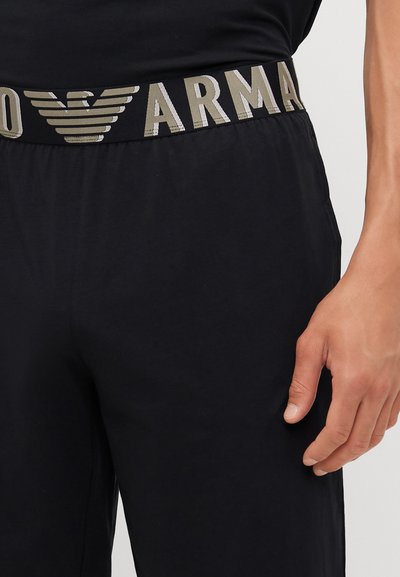 Pantaloni sportivi neri con un ampio elastico in vita che presenta un design del logo in oro e argento. Tessuto liscio e vestibilità comoda.