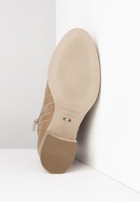 Beige leren enkelboot met een gestructureerde zool en zijrits. Merken en maatdetails zijn op de zool geperst. Glad afwerking.