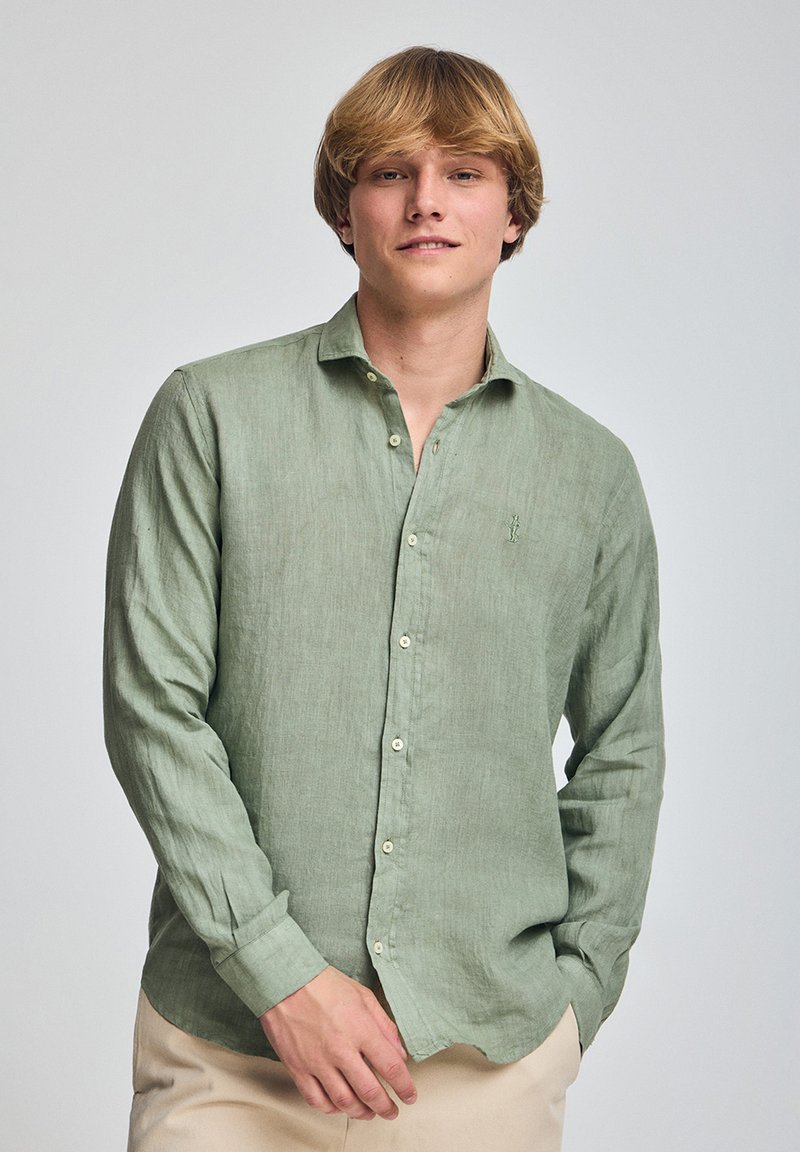 Camicia a maniche lunghe in lino verde chiaro con colletto a punta, chiusura con bottoni sul fronte e dettaglio logo discreto sul petto. Texture liscia.