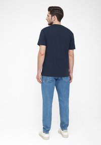Navyblaues T-Shirt mit Rundhalsausschnitt, kurzen Ärmeln und lockerer Passform, kombiniert mit hellblauen Jeans und weißen Sneakers.