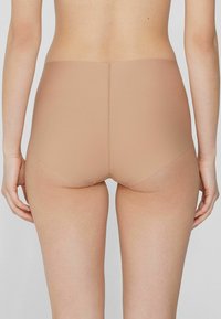 Vysoké nahé spodní prádlo s hladkou texturou materiálu, bezešvou konstrukcí a bez viditelného kování nebo akcentů, z pohledu zezadu.