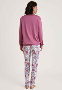 Lange mouw roze top gecombineerd met witte broek met bloemenpatroon, featuring levendige roze, blauwe en groene bloemen. Zacht materiaal, ontspannen pasvorm.