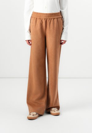 Brown wide-leg pants made of soft fabric with an elastic waistband, paired with patterned beige slippers and a buttoned white shirt.