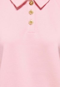 Chemise rose à col ornée de trois boutons dorés en forme de soleil sur la patte de boutonnage devant.