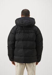 Black puffer jacket with a hood, featuring a quilted design, thick insulation, and a high collar, seen from the back.
