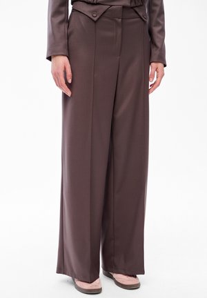 Brązowe szerokie spodnie z wysokim stanem i detalami na guziki, noszone z jasnoróżowymi butami i dopasowaną brązową marynarką.