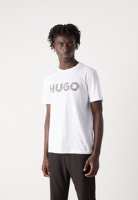 Hvit bomulls t-skjorte med et stort, rutete "HUGO"-logo i svart og grått. Korte ermer, rund hals, avslappet passform.
