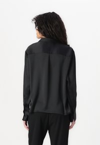 Black satin shirt featuring a classic collar, long sleeves, and a smooth texture. Notable details include button cuffs and a relaxed fit.