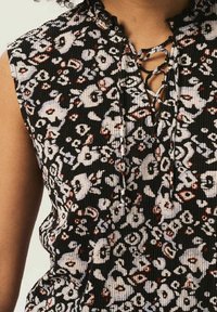 Svart ärmlös topp i texturerat ribbat tyg, med ett blommönster i vitt och röd, med en snörning vid halsringningen.