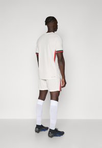 Hvid atletisk trøje med korte ærmer, prydet med røde og grønne detaljer. Sammen med hvide shorts og knæhøje hvide sokker. Sorte fodboldstøvler.