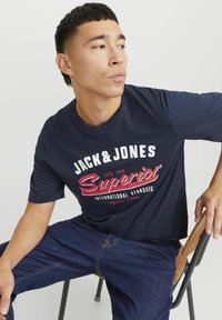 Donkerblauwe katoenen t-shirt met korte mouwen en een grote grafische print in wit en rood, gecombineerd met donkere spijkerbroek.