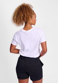 Hvid bomulds t-shirt med korte ærmer, parret med sorte shorts med elastisk talje. Struktureret krøllet hår synligt, set bagfra.