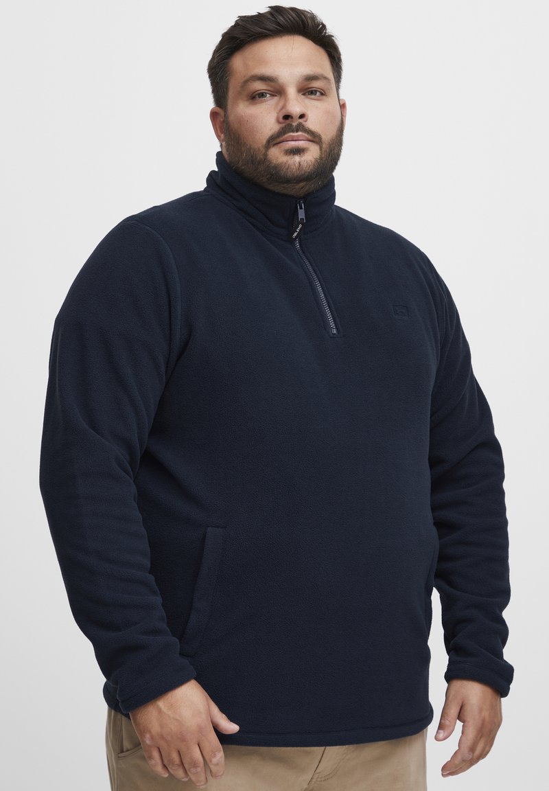 Pullover in pile blu navy da uomo, con colletto alto, zip parziale frontale e tasche laterali; texture morbida con un design semplice e un colore uniforme.