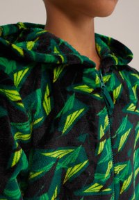 Fleece zip-up kapuca s črno osnovo in zelenimi listnimi vzorci, strukturno blago in kapuco. Zadrga je na sredini spredaj.