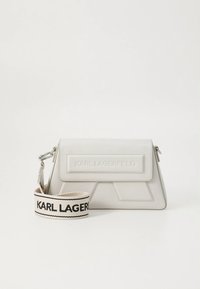 Άσπρη τσάντα χειρός από ψεύτικο δέρμα με δομημένο σχέδιο, που διαθέτει μπροστινό καπάκι και ανάγλυφο λογότυπο, συνοδευόμενη από πλεκτό λουράκι με το όνομα της μάρκας.