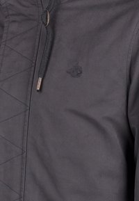 Svart jacka med kviltad design, dragsko i huven och diskret logotyp. Slät textur med metalldetaljer.