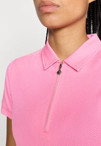 Roza polo majica iz teksturirane tkanine, z zadrgo na ovratniku in kratkimi rokavi. Nežen vzorec dodaja globino oblikovanju.