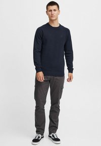Navy knitted sweater with ribbed cuffs and hem; paired with gray cargo pants and black sneakers featuring white laces.
