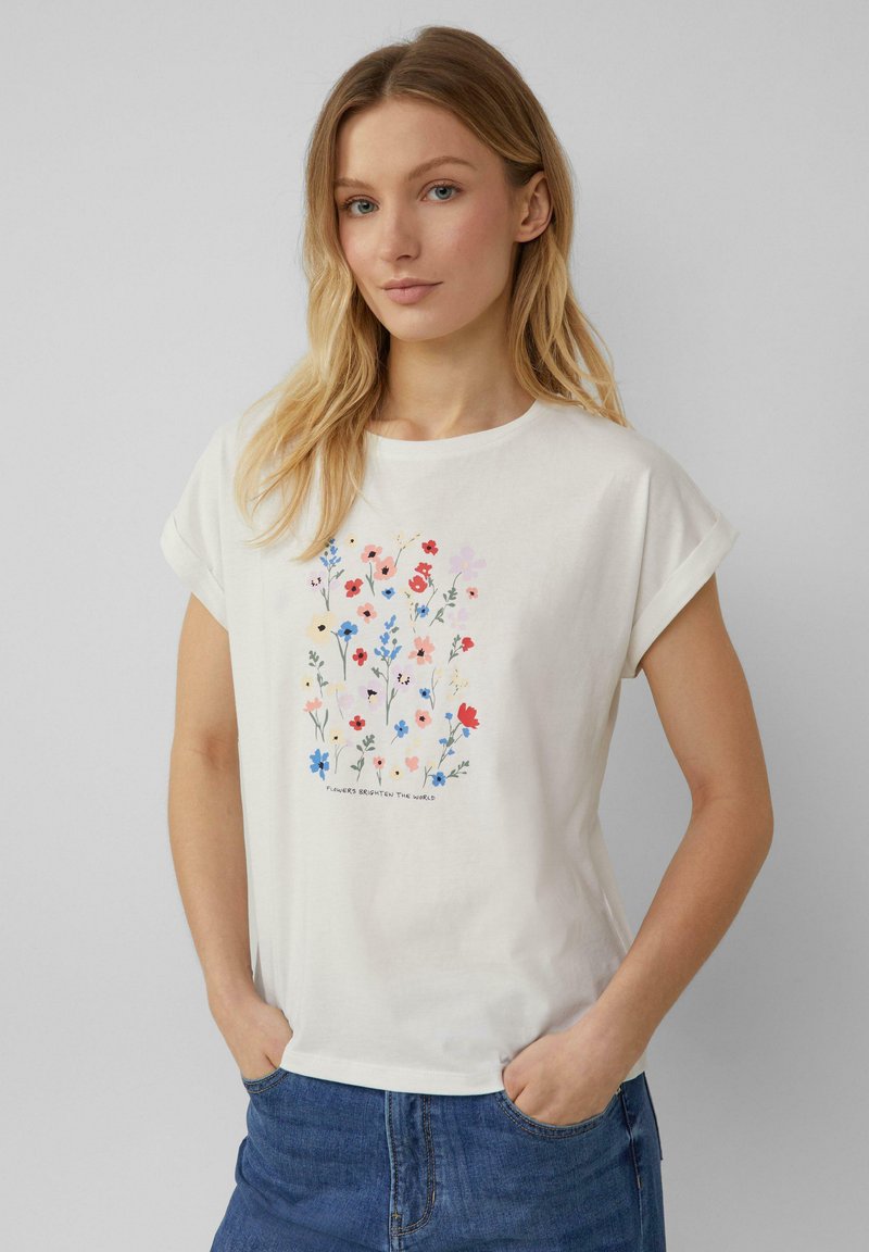 Witte t-shirt met korte mouwen, voorzien van een bloemmotief in verschillende kleuren, met onderaan de tekst: "Bloemen verlichten de wereld."