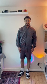 Herre lett, grå hettejakke med glidelås og elastiske mansjetter, kombinert med matchende shorts. Har svarte sneakers og hvite anklestømper.